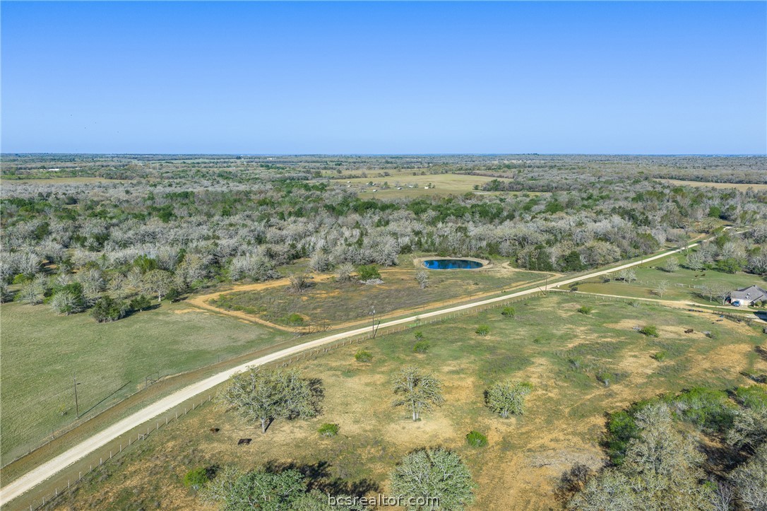 Aerial view of rural acreage with a pond, pasture, and tree-lined road.