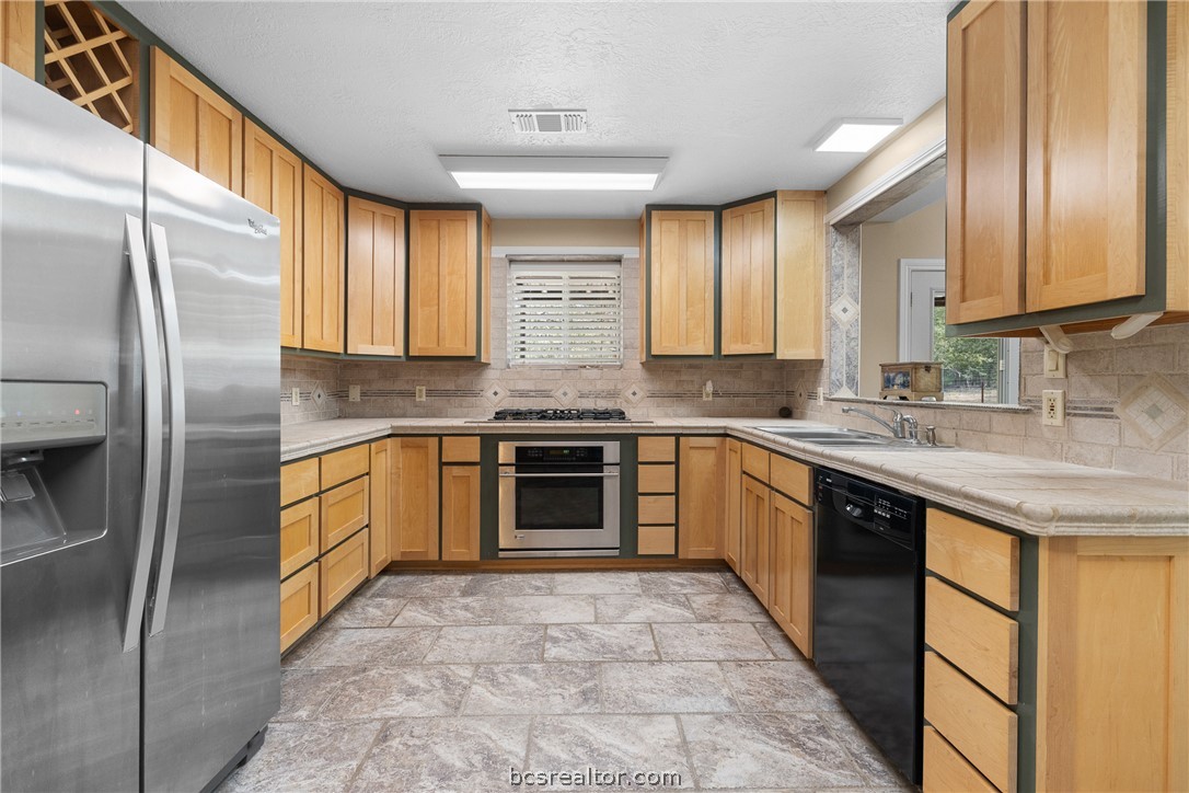 Kitchen with honey-colored wood cabinets, stone-look counters, and stainless steel and black appliances.