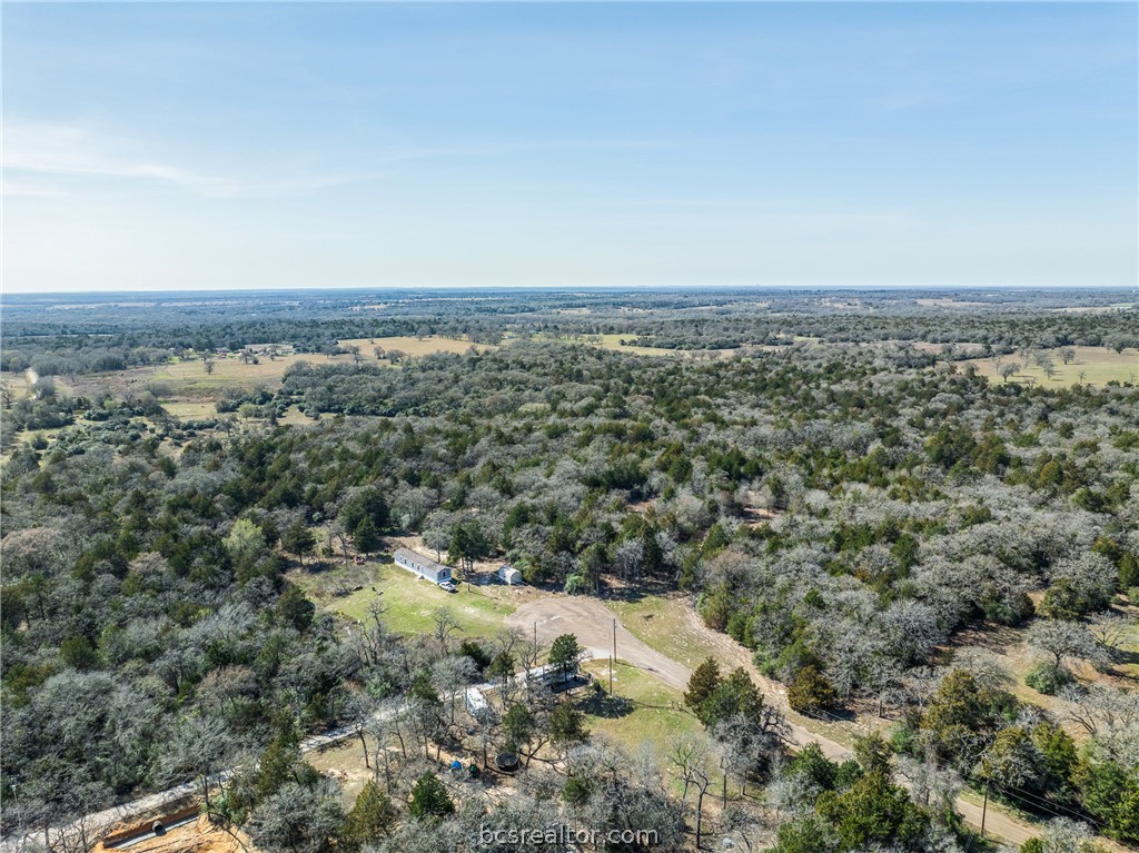 Aerial view of wooded acreage with a small house, outbuilding, and cleared driveway.