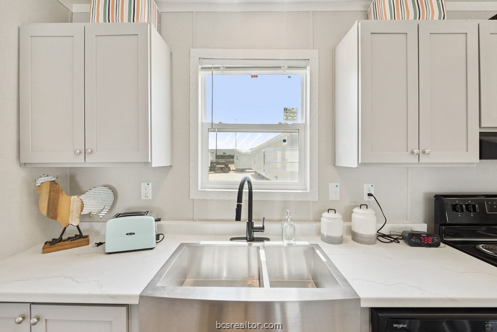 Kitchen with white cabinets, a large stainless-steel sink, and a window above the faucet.