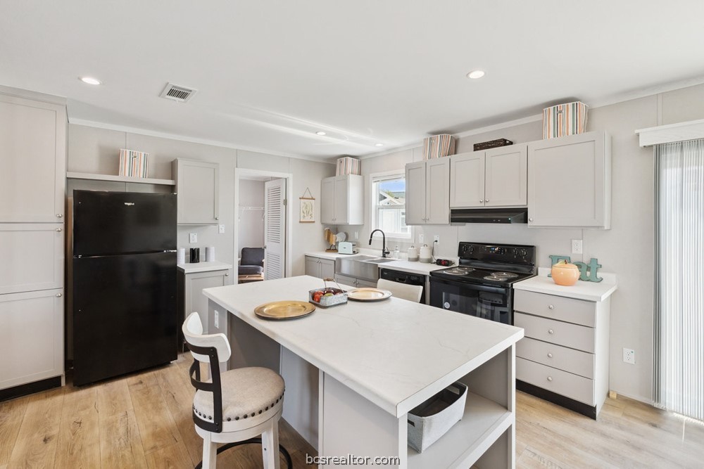 Kitchen with a large white island, black appliances, and light wood-look flooring.