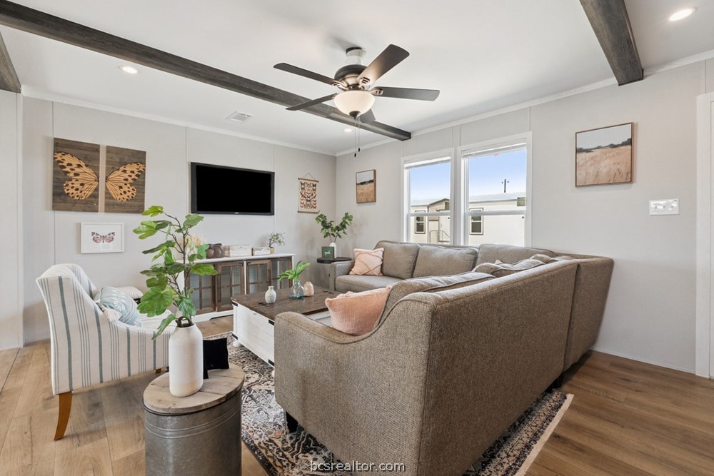 Living room with a gray sectional, striped armchair, dark ceiling beams, and tall windows.