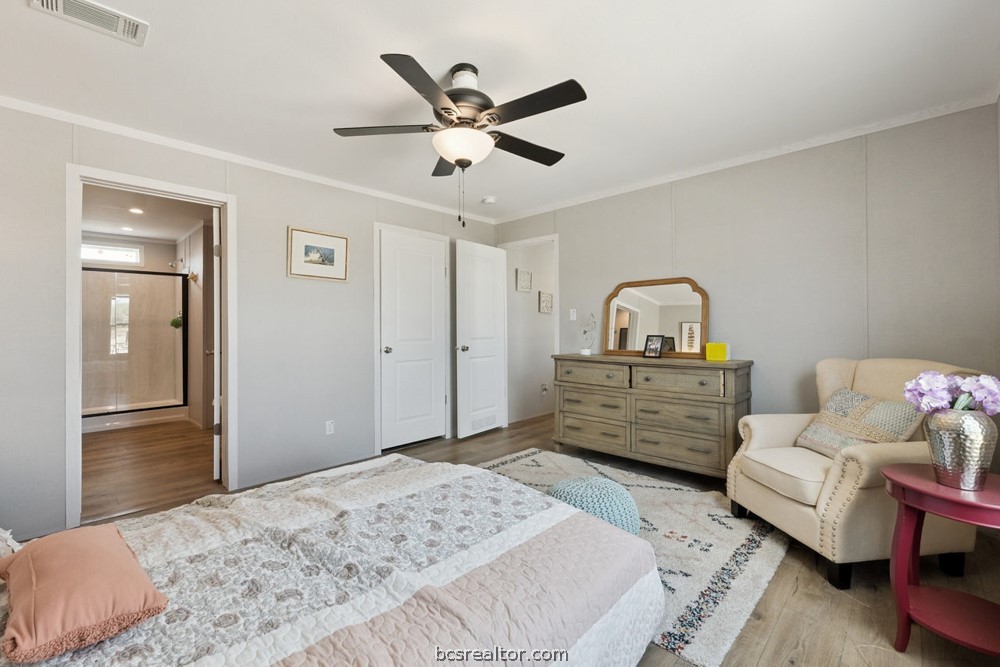 Furnished bedroom with a large bed, ceiling fan, and open doorway to a bathroom.