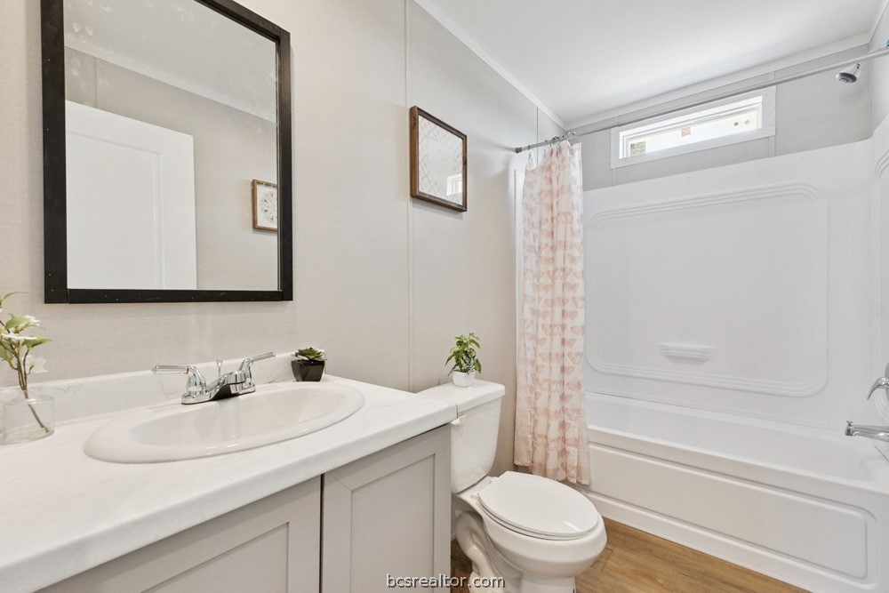 Bathroom with a white vanity, large framed mirror, and tub-shower with a pink patterned curtain.