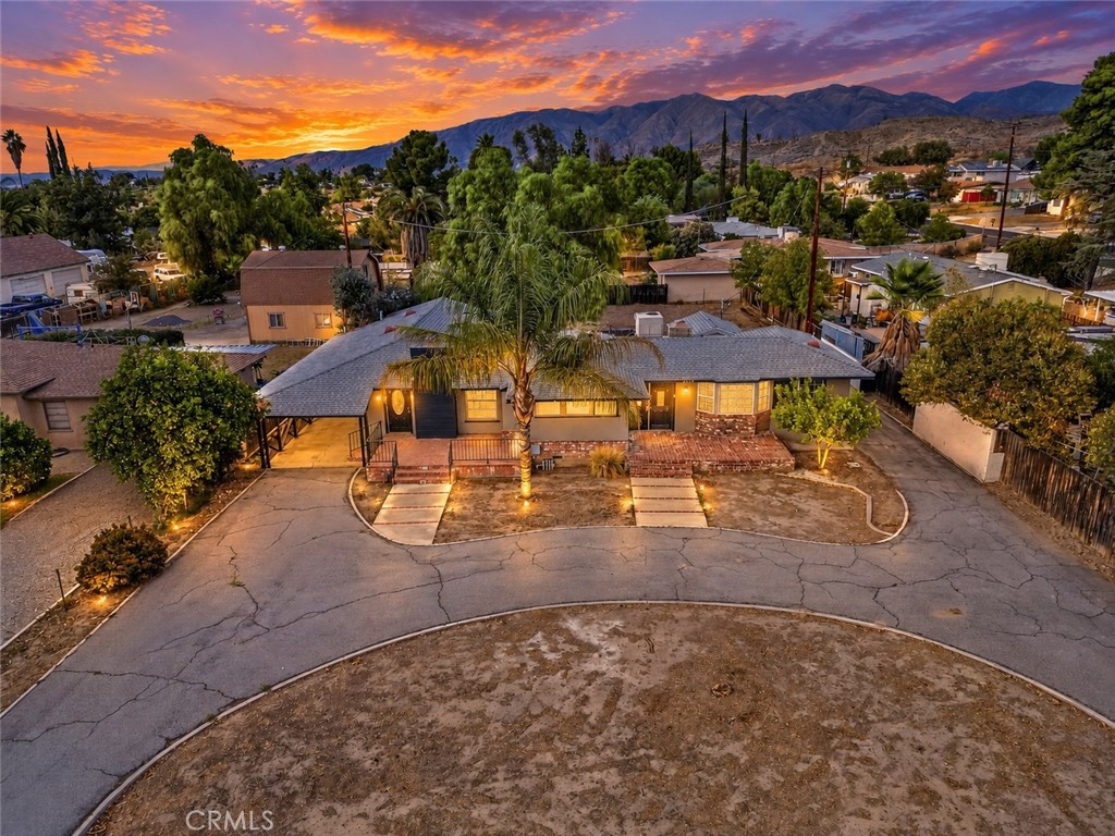 Single-story home with a broad curved driveway, palm trees, and mountains at sunset.