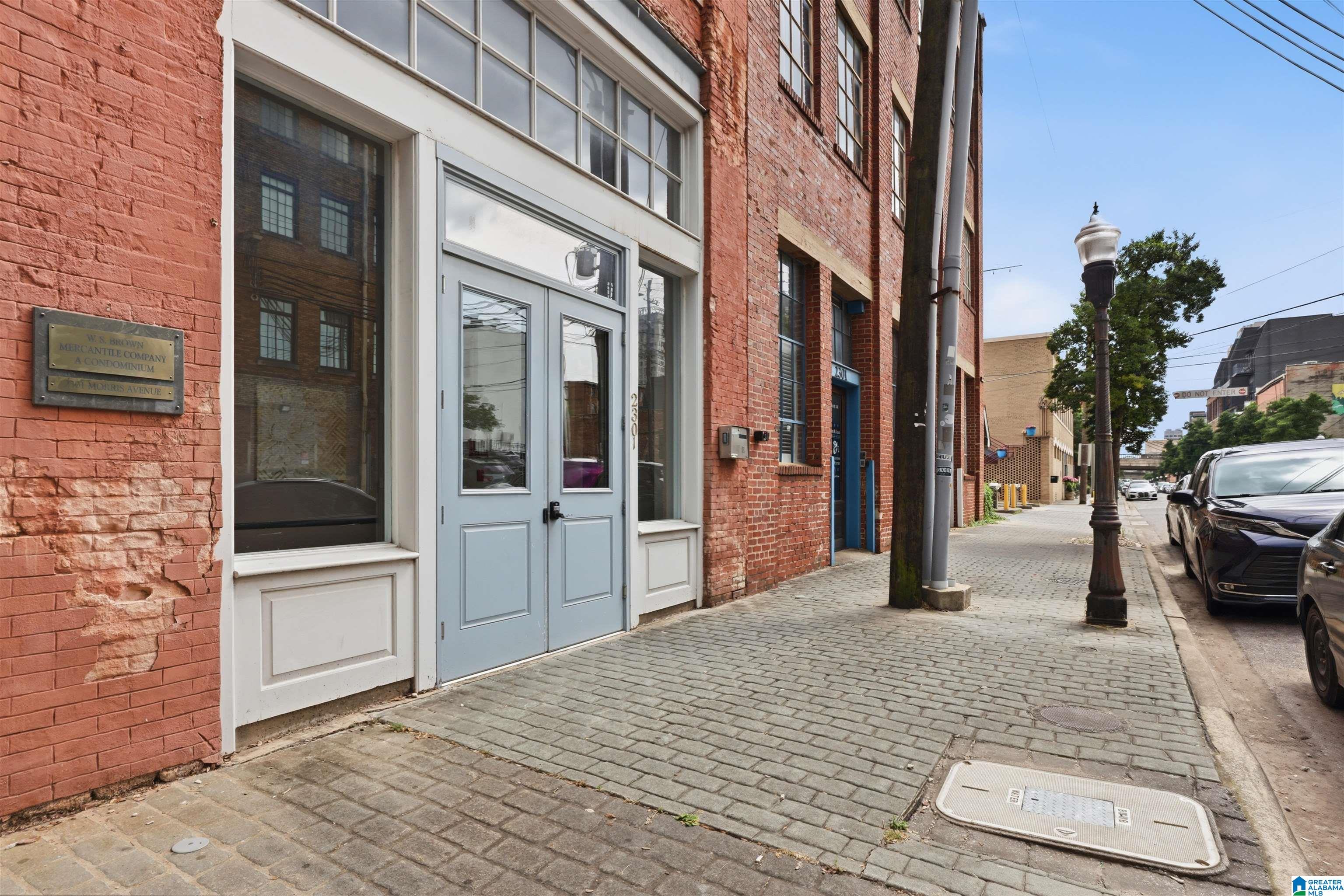 Red-brick condominium entrance with pale blue doors beside a cobblestone sidewalk.