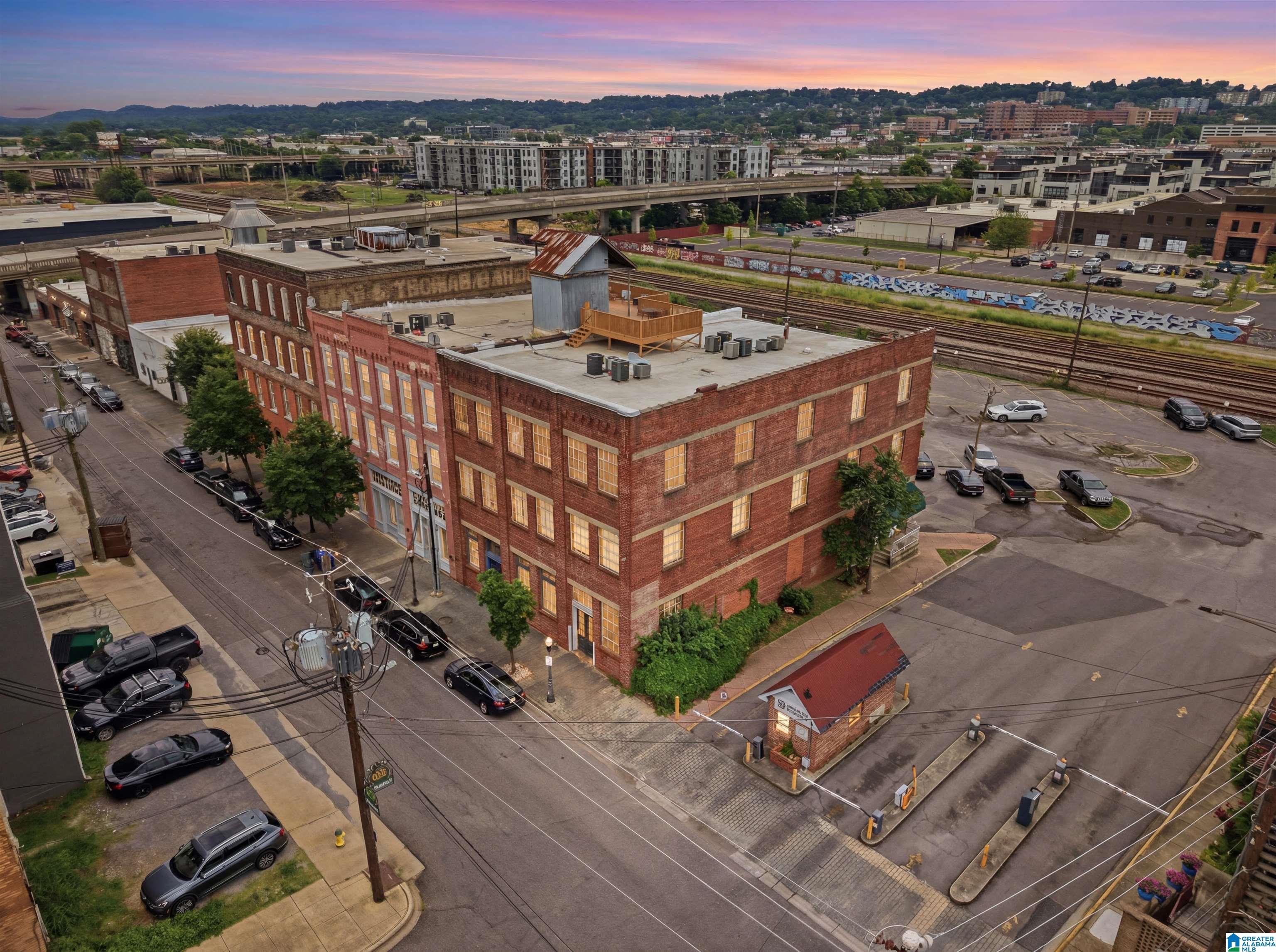 Aerial view of a four-story red-brick building beside railroad tracks at dusk.