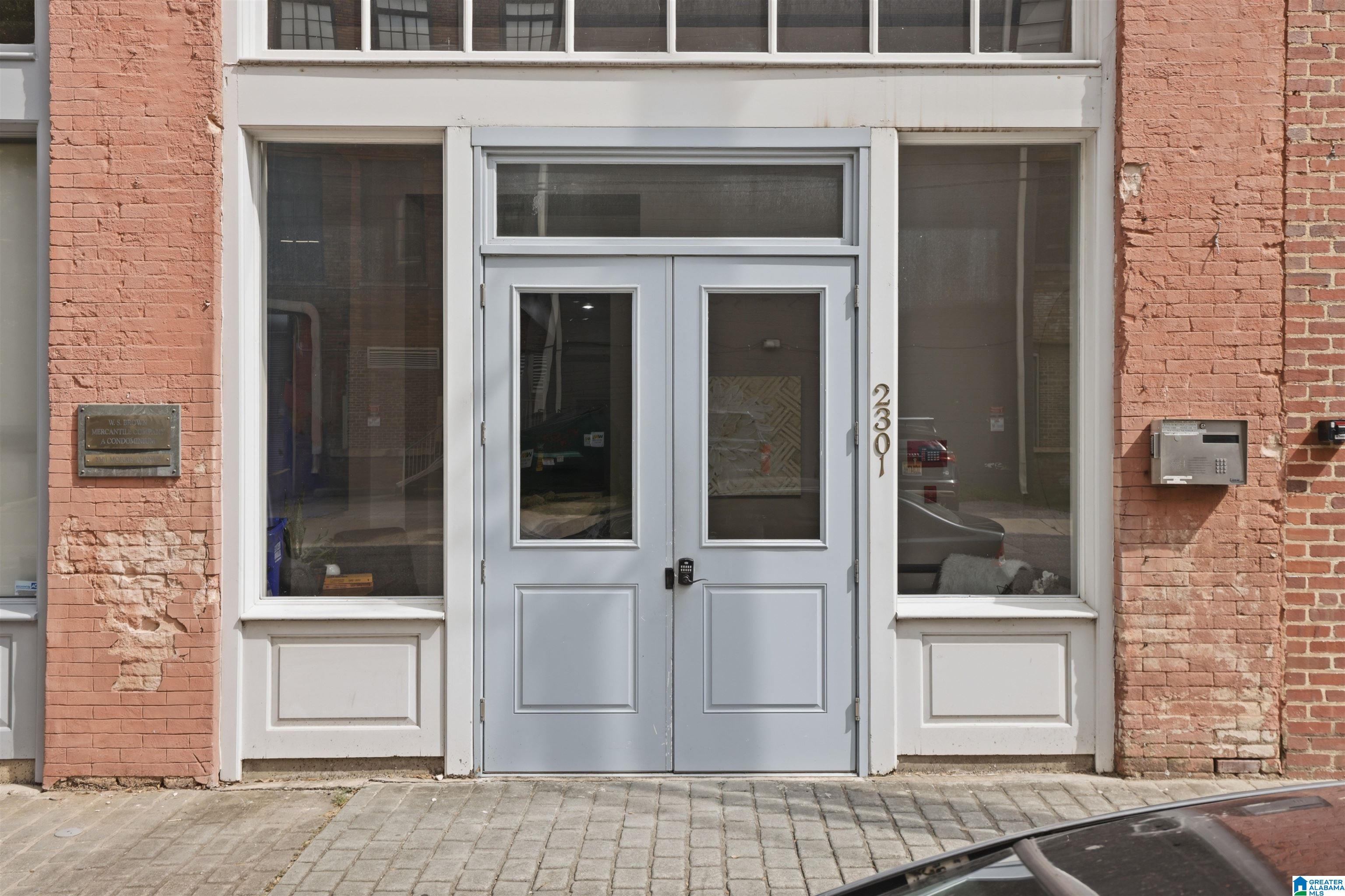 Brick condominium entrance with gray double doors, glass sidelights, and 2301 address numerals.