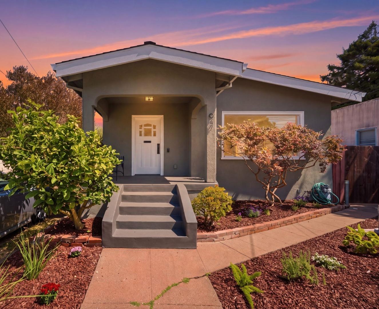 Gray single-story home with recessed white entry, broad steps, and landscaped garden at sunset.