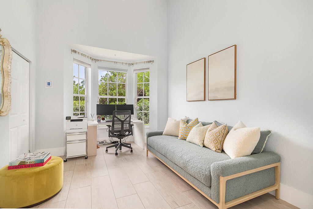 Furnished home office with a window-bay desk, gray sofa, and yellow ottoman.
