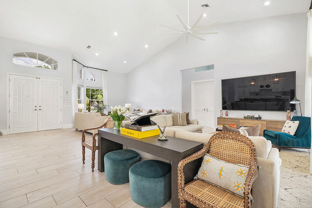 Furnished living room with a vaulted ceiling, large fan, wall-mounted television, and teal accent chairs.