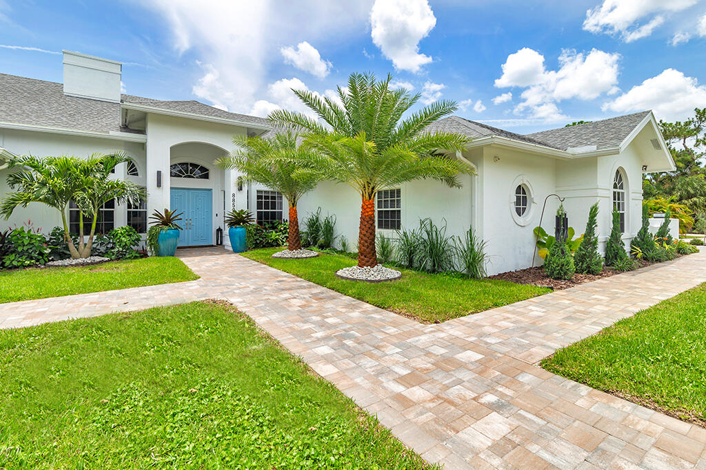White single-story home with a blue front door, palm trees, and a branching stone-paver walkway.