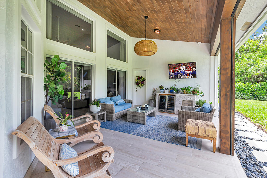 Covered patio with wicker seating, blue cushions, and a wood-plank ceiling beside the garden.