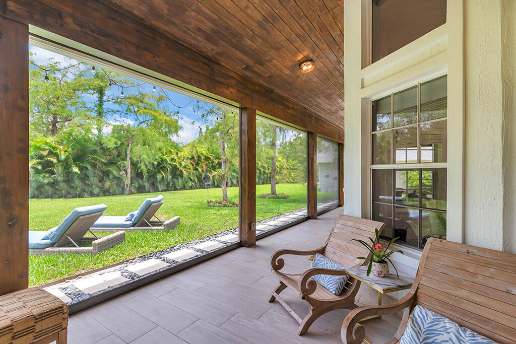Covered patio with wooden seating and a wood ceiling overlooking a tropical lawn.