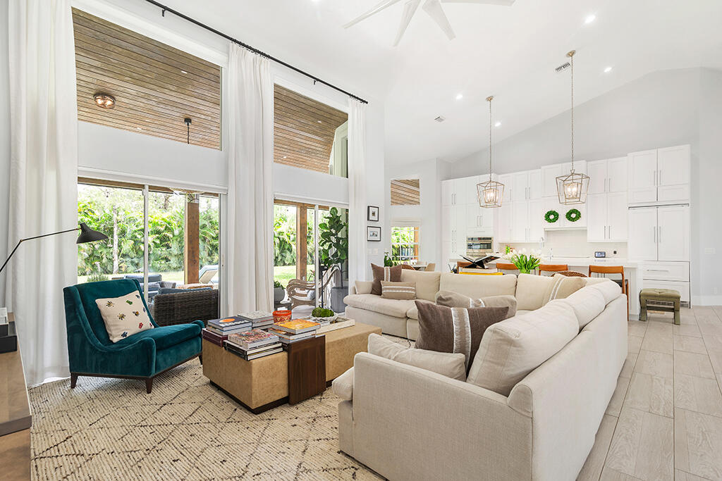 Double-height living room with cream sectional, teal chair, and large windows overlooking greenery.