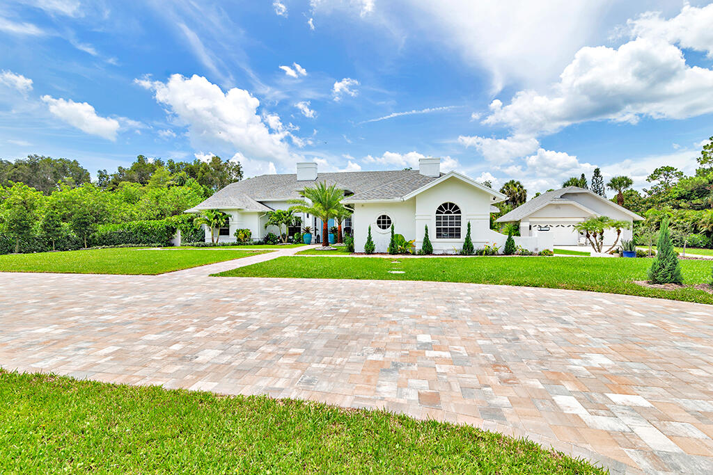 White single-story house with an arched window, palm landscaping, and a broad stone driveway.