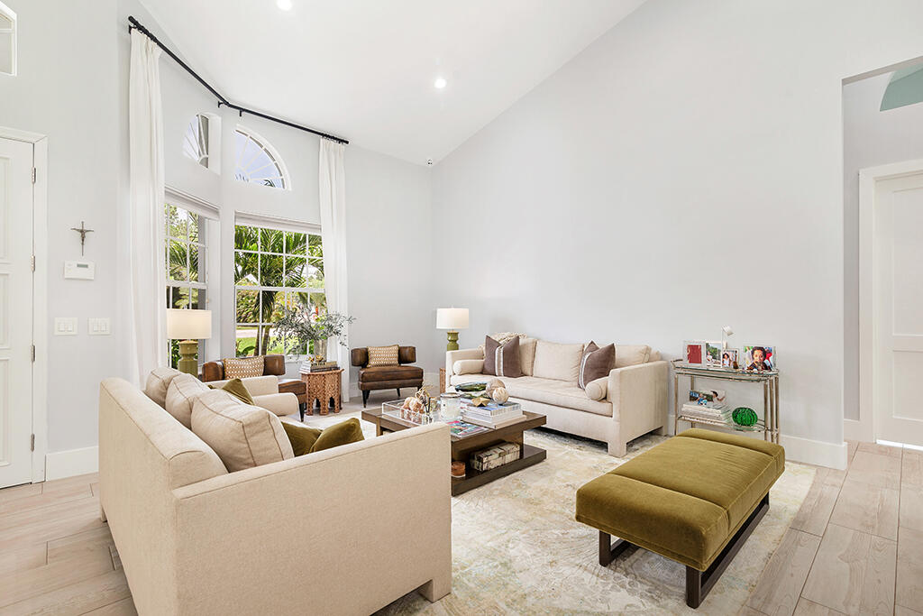 Living room with vaulted ceilings, arched windows, cream sofas, and an olive-green ottoman.