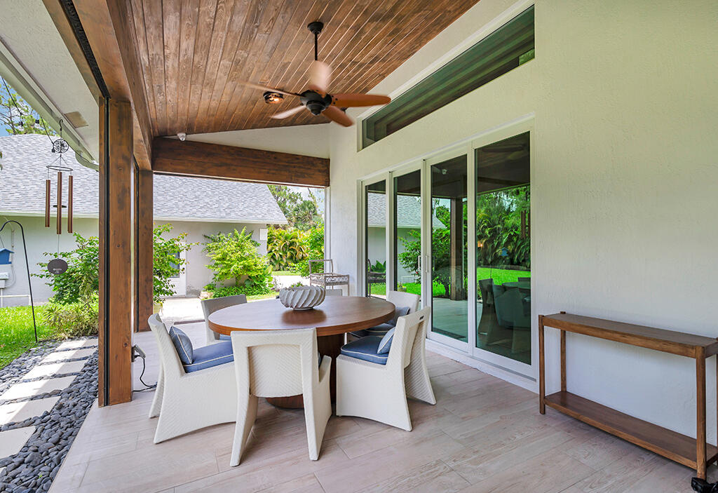 Covered patio with wood ceiling, ceiling fan, and round dining table beside sliding glass doors.