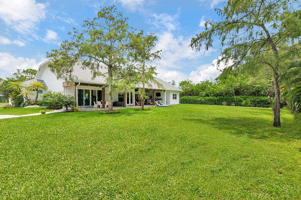 White single-story home with a broad covered patio, viewed across a spacious green backyard.