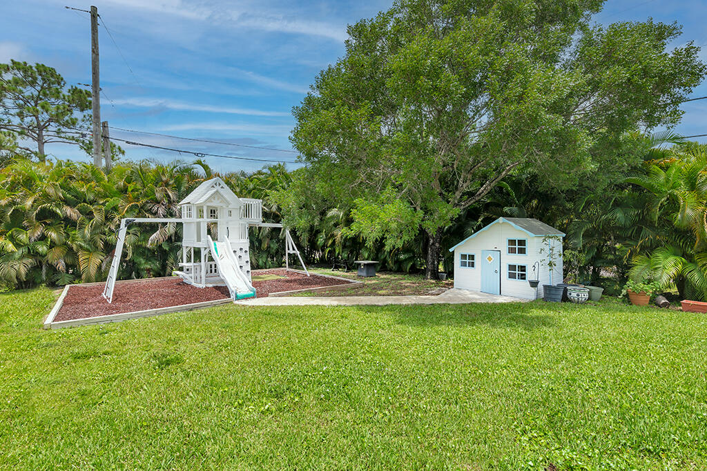 Backyard with a white playset, small shed, broad lawn, and large shade tree.