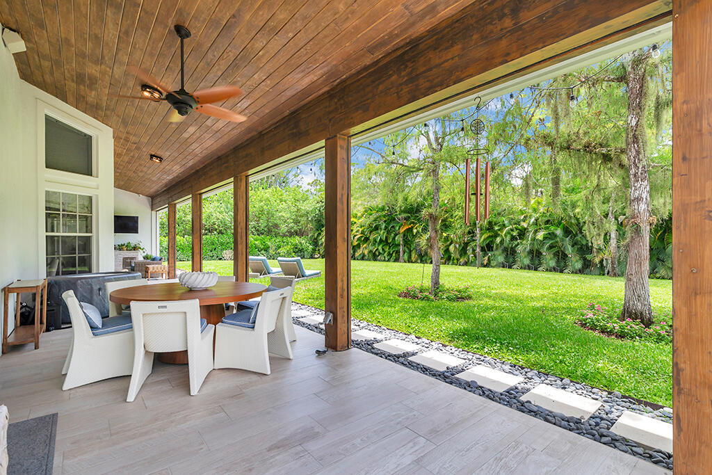 Covered patio with a wood ceiling and dining set overlooking a green lawn and mature trees.