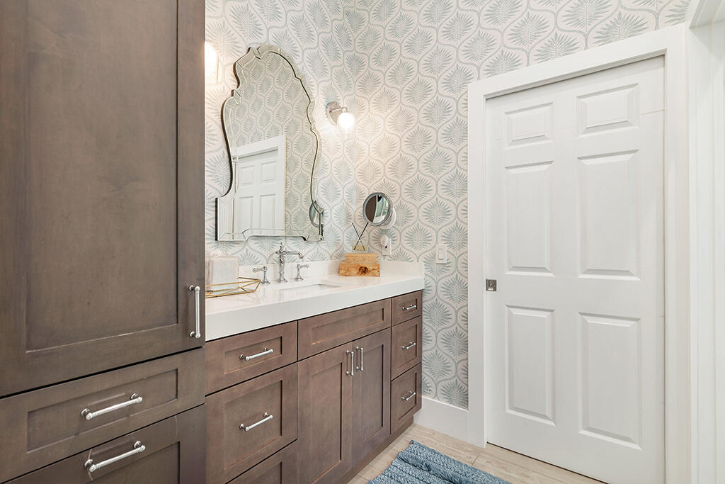 Bathroom vanity with dark wood cabinets, patterned wallpaper, and an ornate mirror.