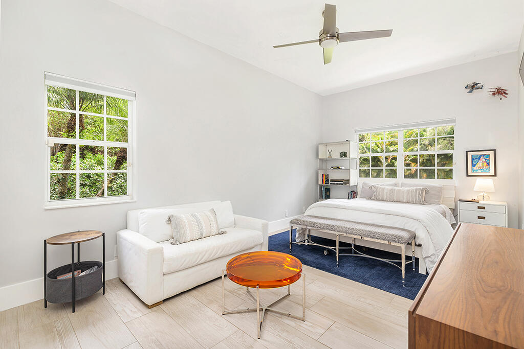 Bright bedroom with a white bed, sofa, navy rug, and windows overlooking greenery.