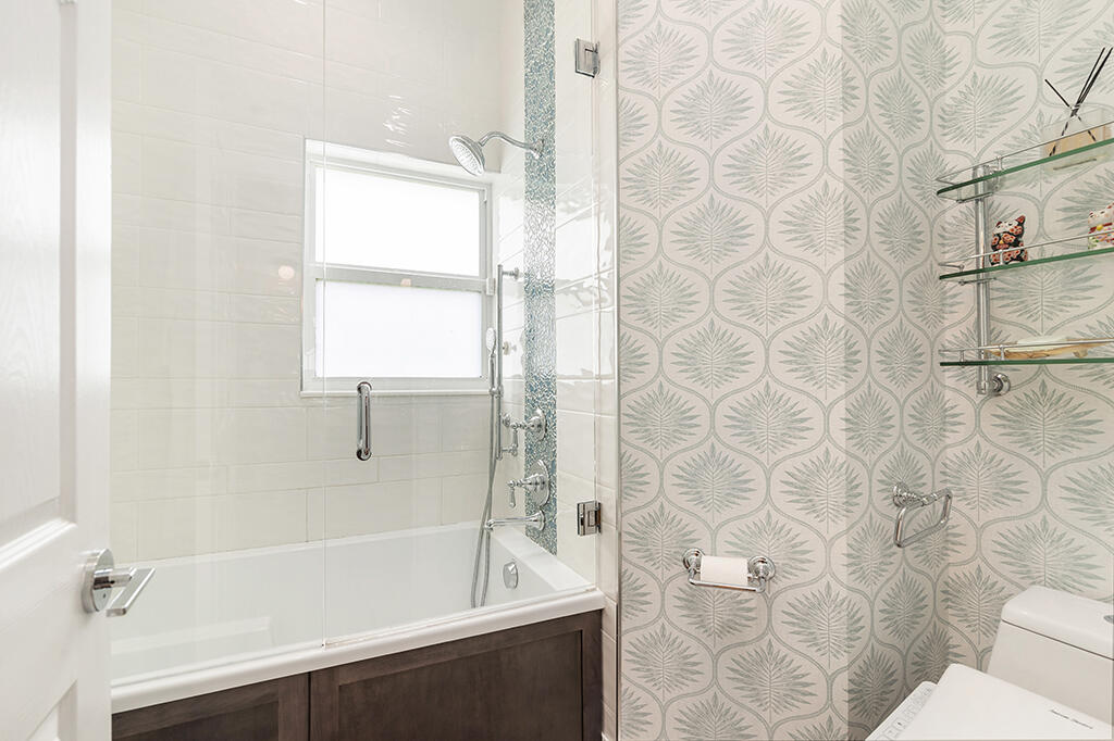 Bathroom with a glass-enclosed bathtub, frosted window, and pale botanical-patterned accent wall.