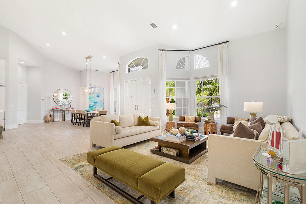 Bright living room with high ceilings, arched windows, cream sofas, and an olive-green ottoman.