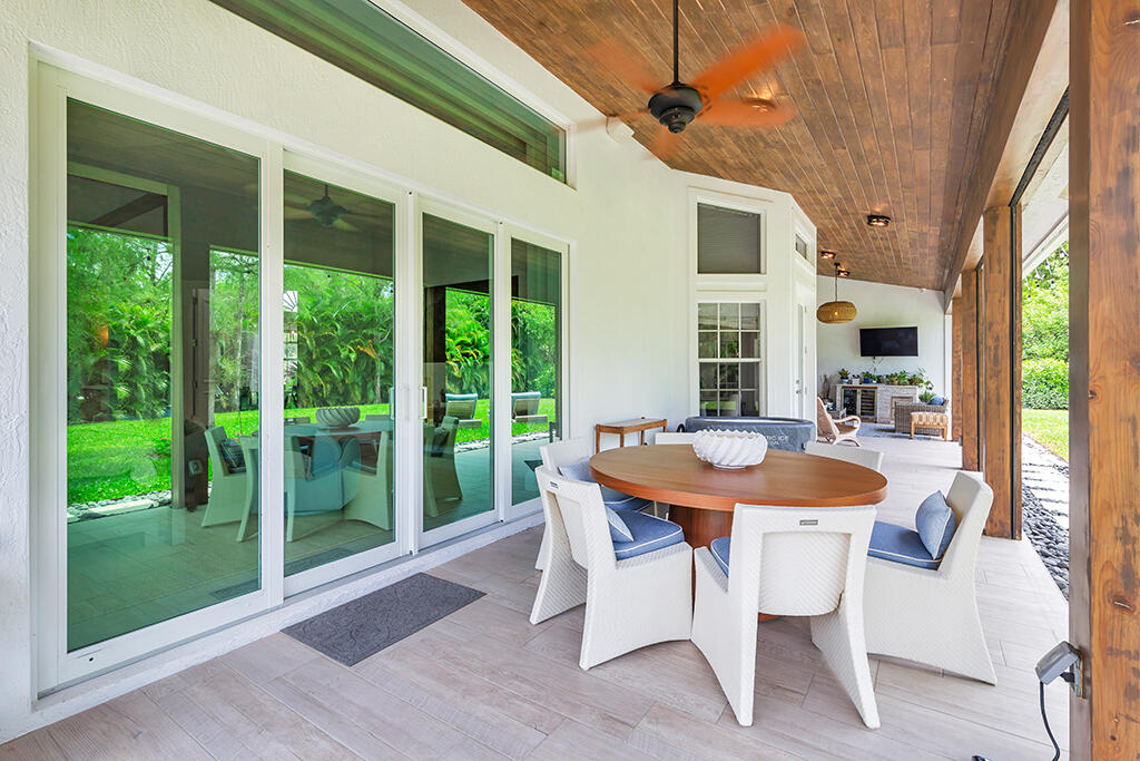 Covered patio with round dining table, white chairs, wood ceiling, and views of the garden.
