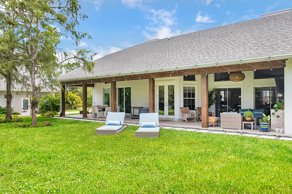 Home’s covered rear patio with outdoor seating, string lights, and a broad green lawn.