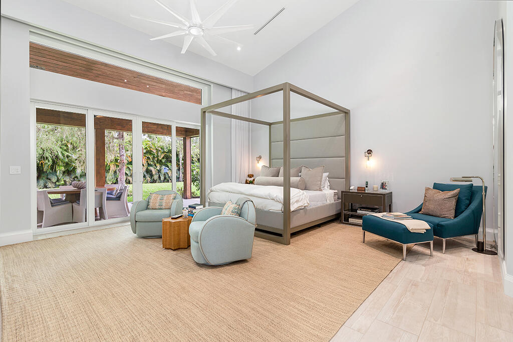 Bedroom with an upholstered canopy bed, blue lounge chairs, and sliding glass doors to a garden patio.