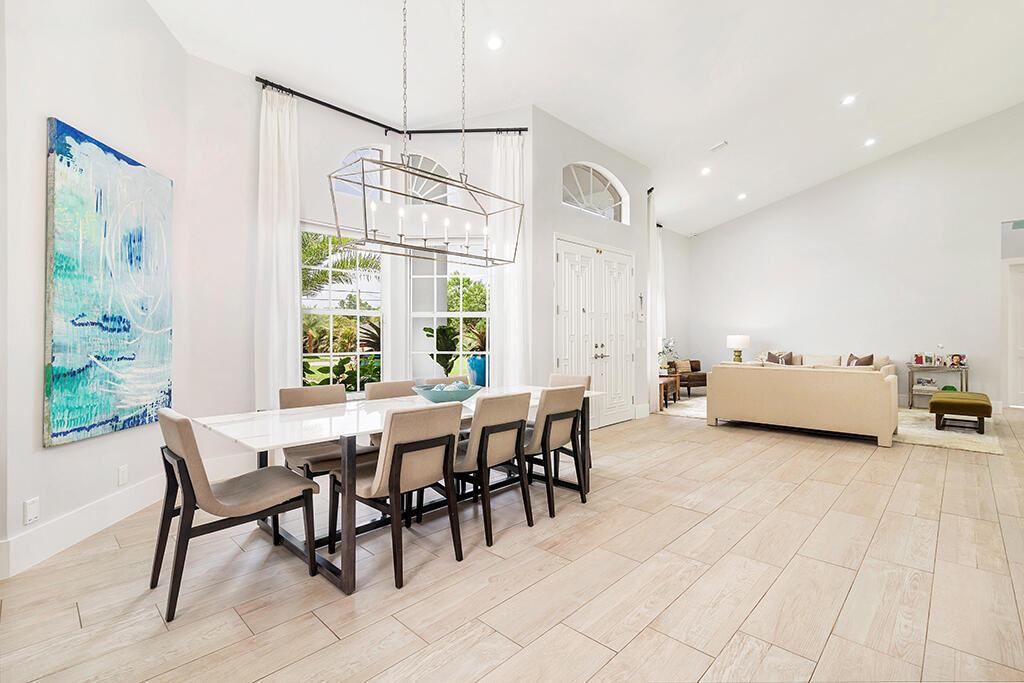 Open-plan dining and living room with a long table, tall windows, and light tile flooring.