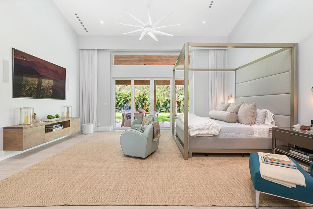 Bright bedroom with a canopy bed, pale blue armchair, and glass doors overlooking a lush garden.