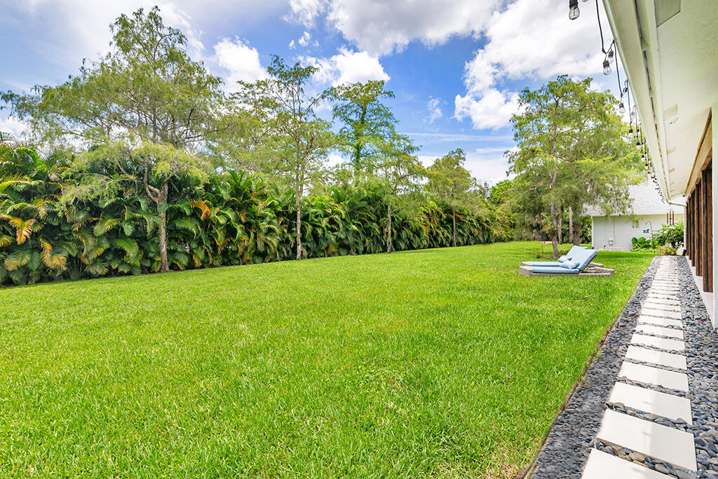 Spacious lawn bordered by palms, with lounge chairs and a stepping-stone path beside the house.