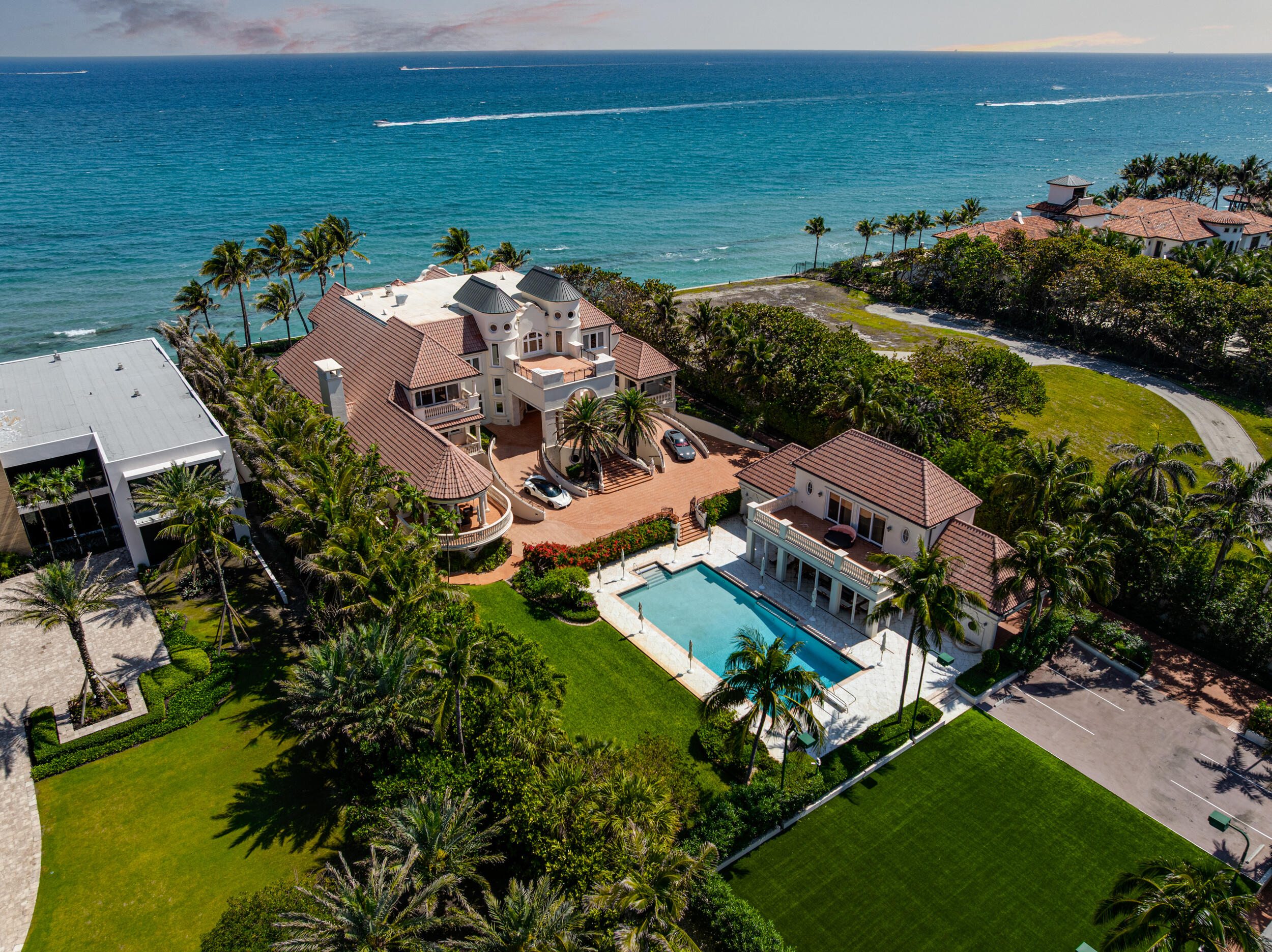 Oceanfront estate with a pool, terracotta roofs, palm trees, and manicured lawns.
