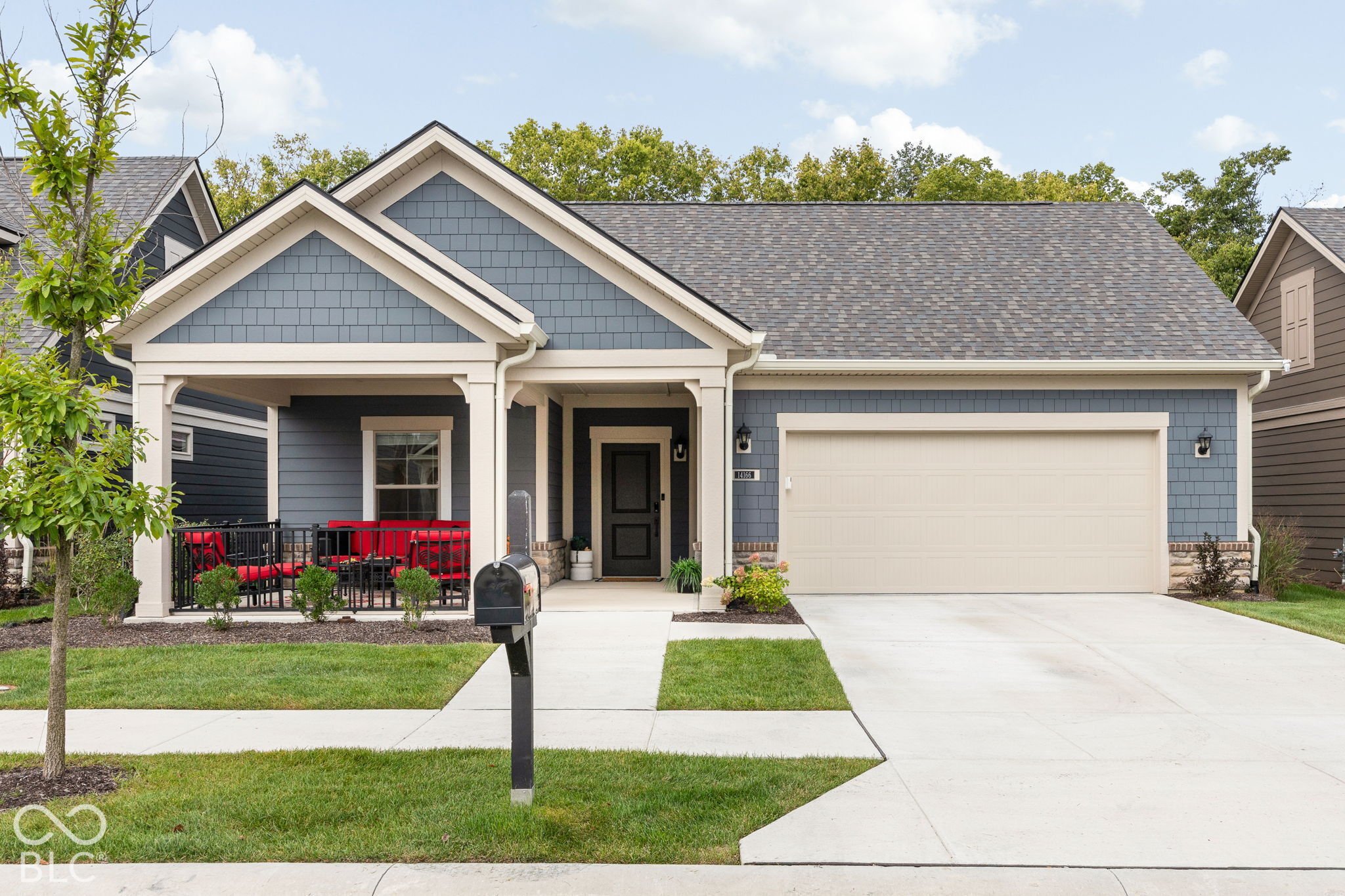 Blue-gray home with white gables, a two-car garage, and a covered porch with red seating.