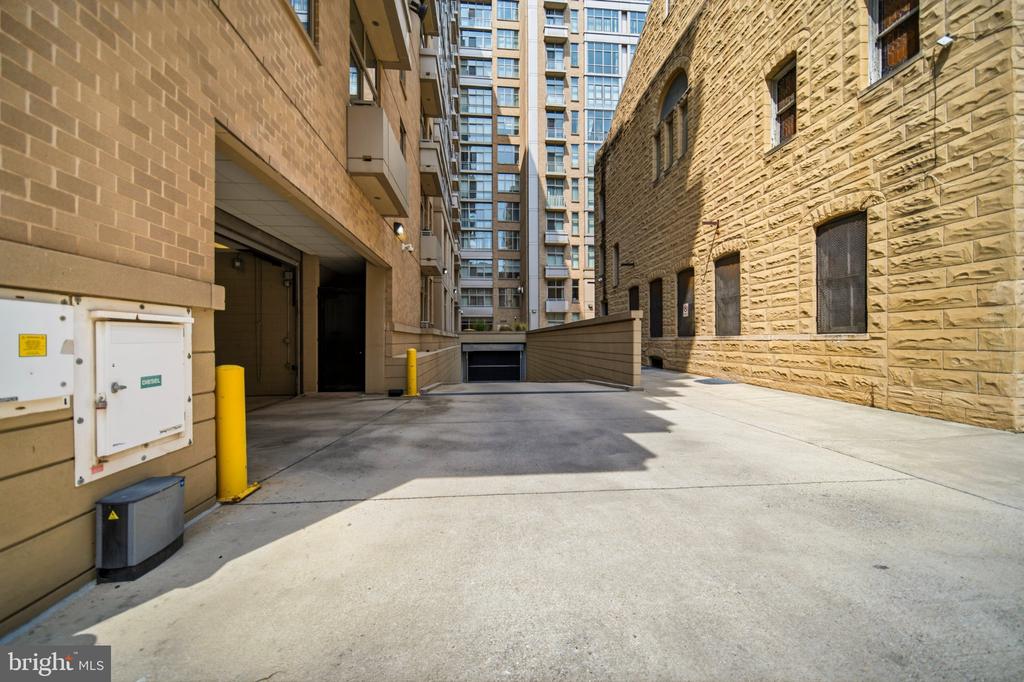 Building exterior with a paved driveway between brick buildings and an underground garage entrance.