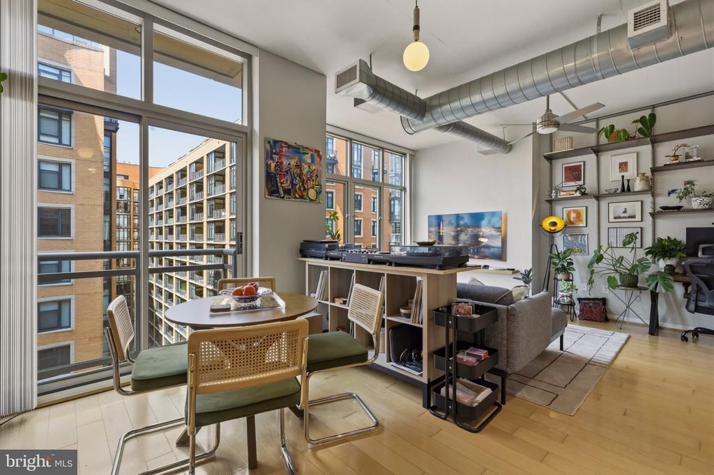 Open-plan condo living and dining area with floor-to-ceiling windows, exposed ductwork, and neighboring building views.