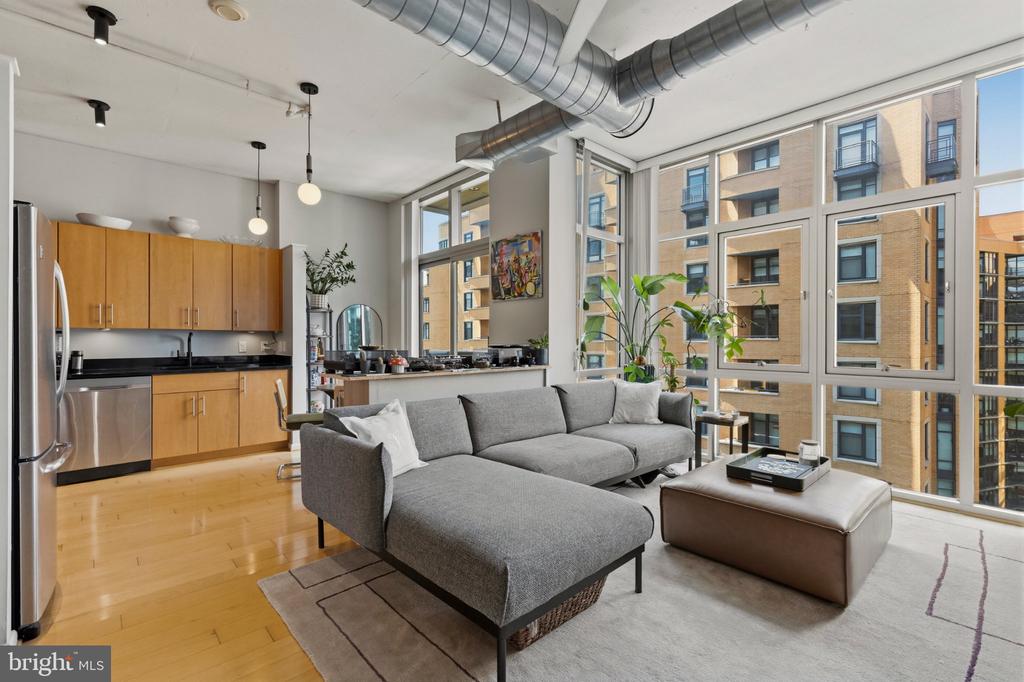 Open-plan condo living room and kitchen with a gray sectional and large city-facing windows.