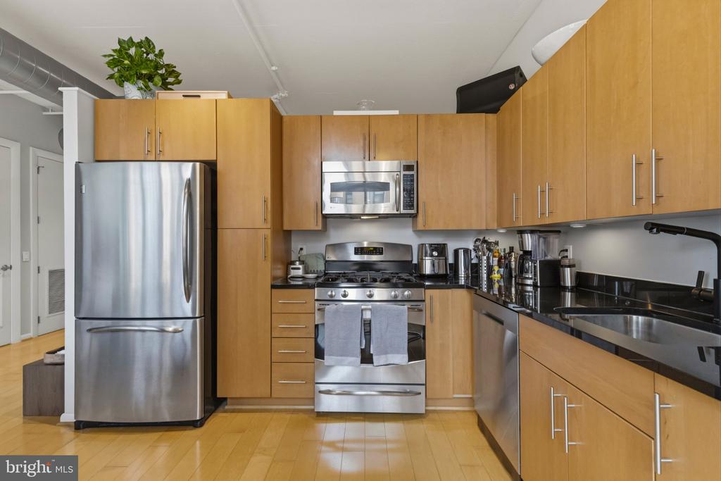 Condominium kitchen with wood cabinetry, black counters, and stainless steel appliances.