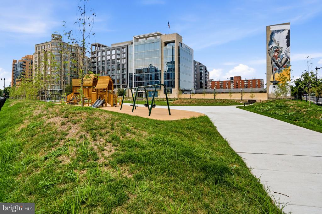 Modern apartment buildings behind a landscaped park with a playground and walking path.