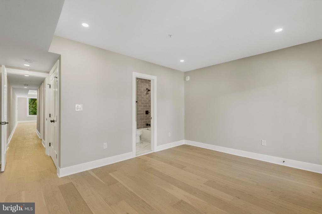 Vacant bedroom with light wood floors, recessed lights, and an open doorway to a tiled bathroom.