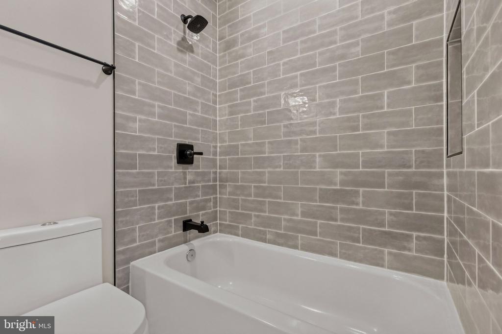 Bathroom with a white tub, gray tile walls, and black shower fixtures.