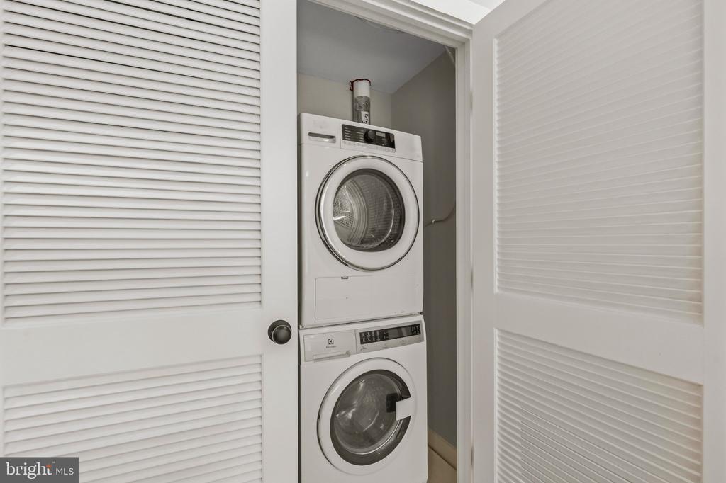 Stacked washer and dryer in a laundry closet behind open louvered doors.