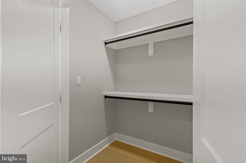 Empty walk-in closet with two shelves, black hanging rods, and a light wood floor.