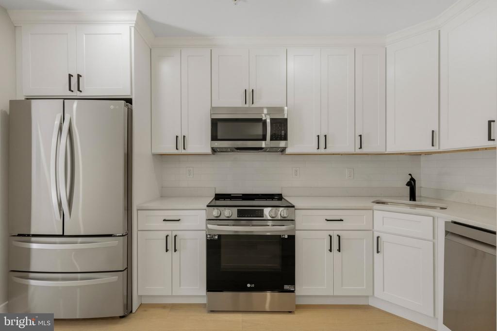 Vacant kitchen with white shaker cabinets, stainless steel appliances, and light wood flooring.