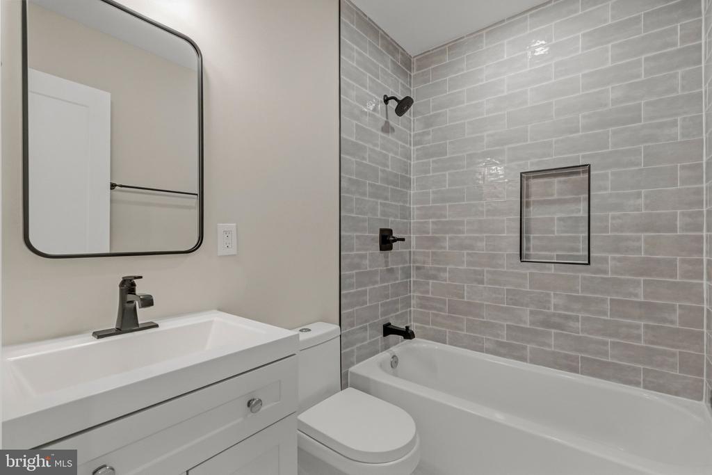 Bathroom with gray tiled tub and shower, white vanity, and black fixtures.