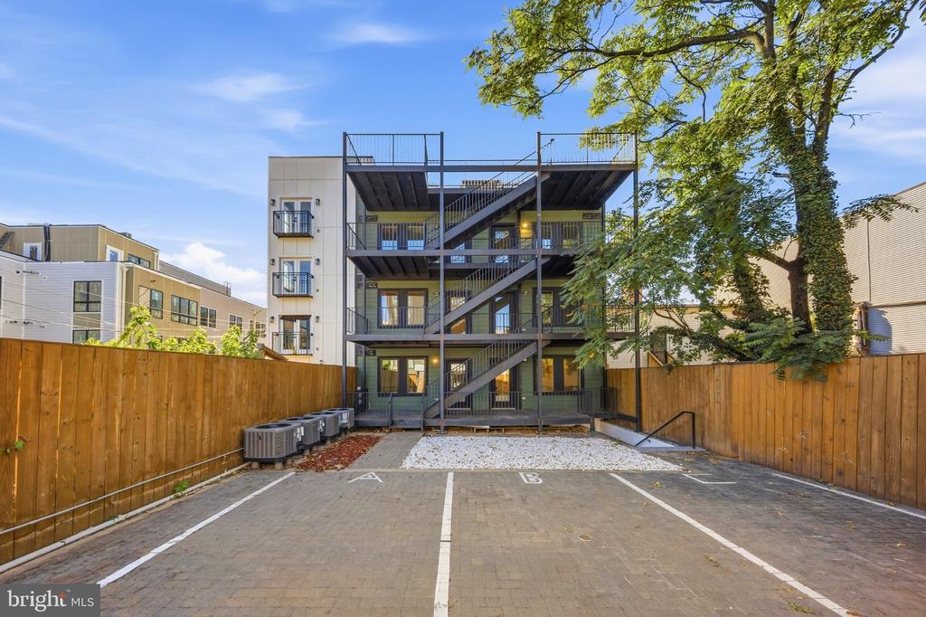 Residential building with black exterior stairs and balconies behind a fenced parking area.