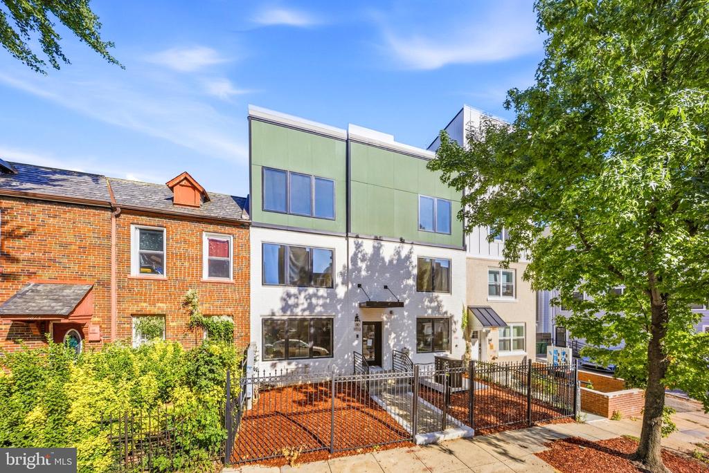 Modern three-story residence with green upper-story panels and a fenced front yard.